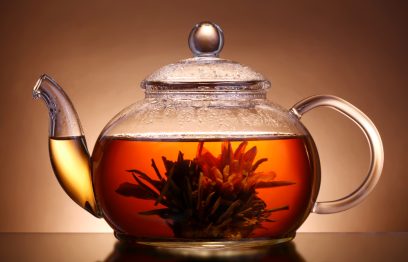 A glass teapot three quarters full of tea. It also has a flower in it.