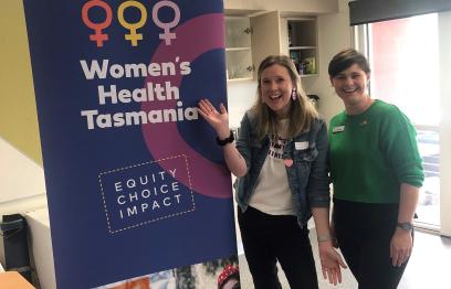 Two of our trainers standing in front of Women's Health Tasmania banner