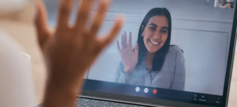 A woman on a computer screen waving and a hand waving in response.