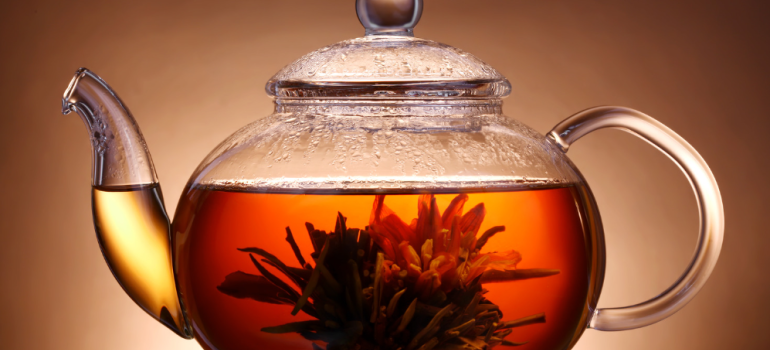 A glass teapot three quarters full of tea. It also has a flower in it.