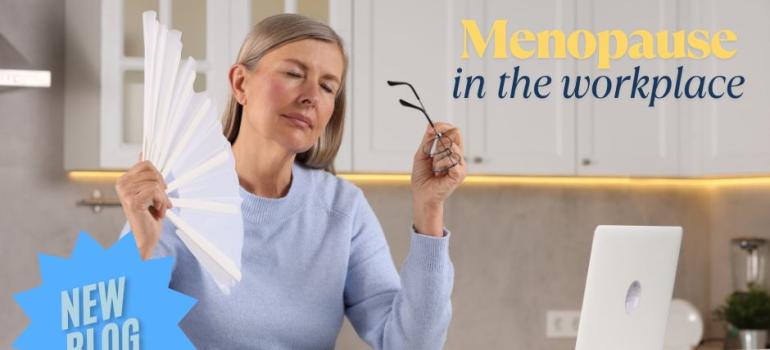 A woman sitting at her laptop cooling herself with a fan.